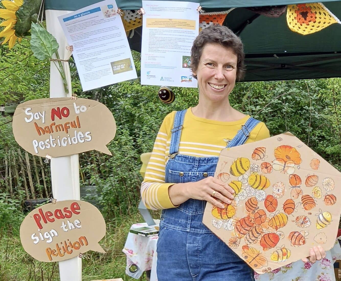 Image of Polly, new Eco Diocese Officer, at a stall holding a cardboard sign protesting against using pesticides.