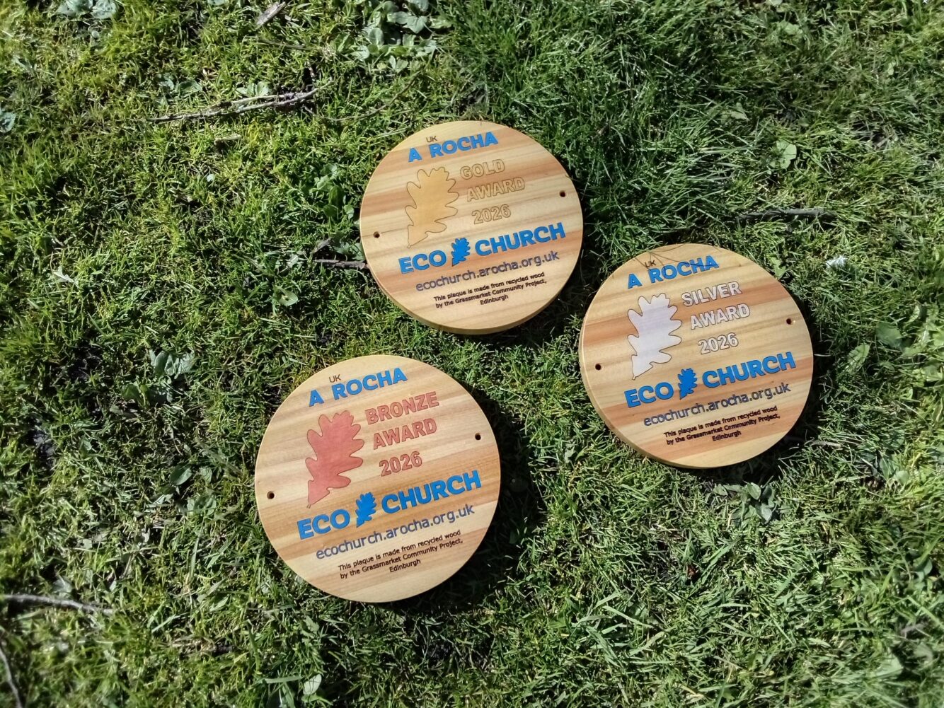 Three round, wooden Eco Church award plaques for Bronze, Silver, and Gold awards achieved in 2026.